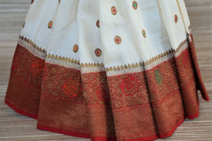 Shop traditional off-white muga Banarasi saree online in USA with antique zari minakari red border and buta. Be a vision of tradition and elegance on weddings and festivals with exquisite Banarasi silk sarees, pure silk sarees, handwoven sarees from Pure Elegance Indian clothing store in USA.-pleats