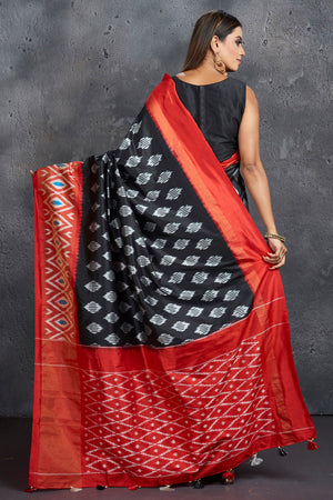 Shop stunning black ikkat silk sari online in USA with red ikkat border. Keep your ethnic wardrobe up to date with latest designer sarees, pure silk sarees, Kanchipuram silk sarees, handwoven sarees, tussar silk sarees, embroidered sarees from Pure Elegance Indian saree store in USA.-back