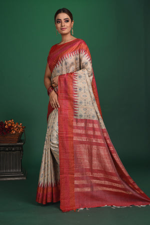 Shop this exquisite beige tussar saree with red vidharbha and zari border online in USA which is handcrafted from fine silk tussar fabric, this tie and dye saree brings out the nature of flow. This tussar saree with elegant red Vidharbha border is making everyone swoon over it. Make it yours and flaunt a handwoven marvel with minimal jewellery for a casual day outfit. Add this pure tussar saree to your collection from Pure Elegance Indian fashion store in USA.-Side view.