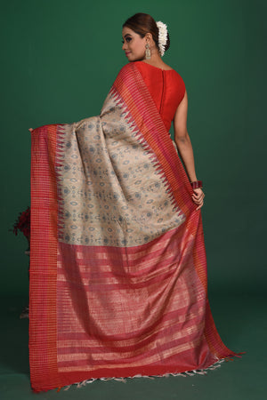 Shop this exquisite beige tussar saree with red vidharbha and zari border online in USA which is handcrafted from fine silk tussar fabric, this tie and dye saree brings out the nature of flow. This tussar saree with elegant red Vidharbha border is making everyone swoon over it. Make it yours and flaunt a handwoven marvel with minimal jewellery for a casual day outfit. Add this pure tussar saree to your collection from Pure Elegance Indian fashion store in USA.-Back view with open pallu.