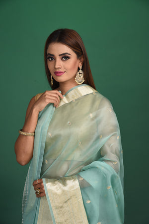 Shop this elegant firozi blue soft organza designer saree with dull gold zari work on heavy border online in USA. Organza silk fabric is a type of silk cloth that is crisp, translucent, and extremely light in weight. It is used to make organza silk saree, drapes, and other decorative pieces. Add this designer sari to your collection from Pure Elegance Indian fashion store in USA.-Close up.