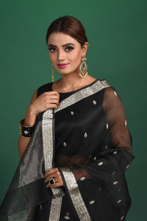 Buy this elegant black soft organza designer saree with silver zari work on heavy border online in USA. Organza silk fabric is a type of silk cloth that is crisp, translucent, and extremely light in weight. It is used to make organza silk saree, drapes, and other decorative pieces. Add this designer sari to your collection from Pure Elegance Indian fashion store in USA.-Close up.