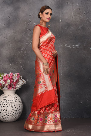 Shop this exquisite coral red silk brocade handloom banarasi saree online in USA. The sari comes with a graceful border with handmade latkan and colourful floral pattern all over. Buy this brocade banarsi sari with zari work from Pure Elegance Indian fashion store in USA and style it with your best pair of heels, gold or Moti necklace and a potli bag for the perfect look.- Side view.