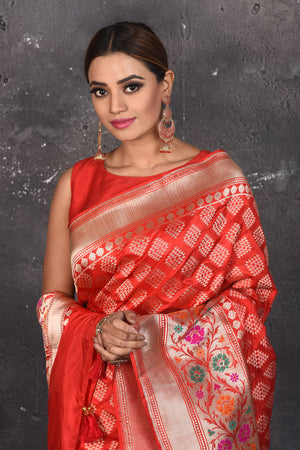Shop this exquisite coral red silk brocade handloom banarasi saree online in USA. The sari comes with a graceful border with handmade latkan and colourful floral pattern all over. Buy this brocade banarsi sari with zari work from Pure Elegance Indian fashion store in USA and style it with your best pair of heels, gold or Moti necklace and a potli bag for the perfect look.- Close up.