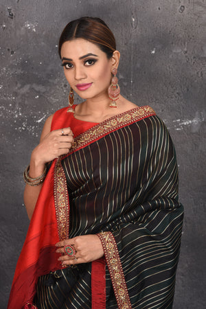 Buy this elegant black saree leheriya with gota patti work online in USA. Style this designer sari which has a beautiful red border with golden lace at the edge with a potli bag and high heels. Add designer gota patti sari to your collection from Pure Elegance Indian saree store in USA.- Close up.