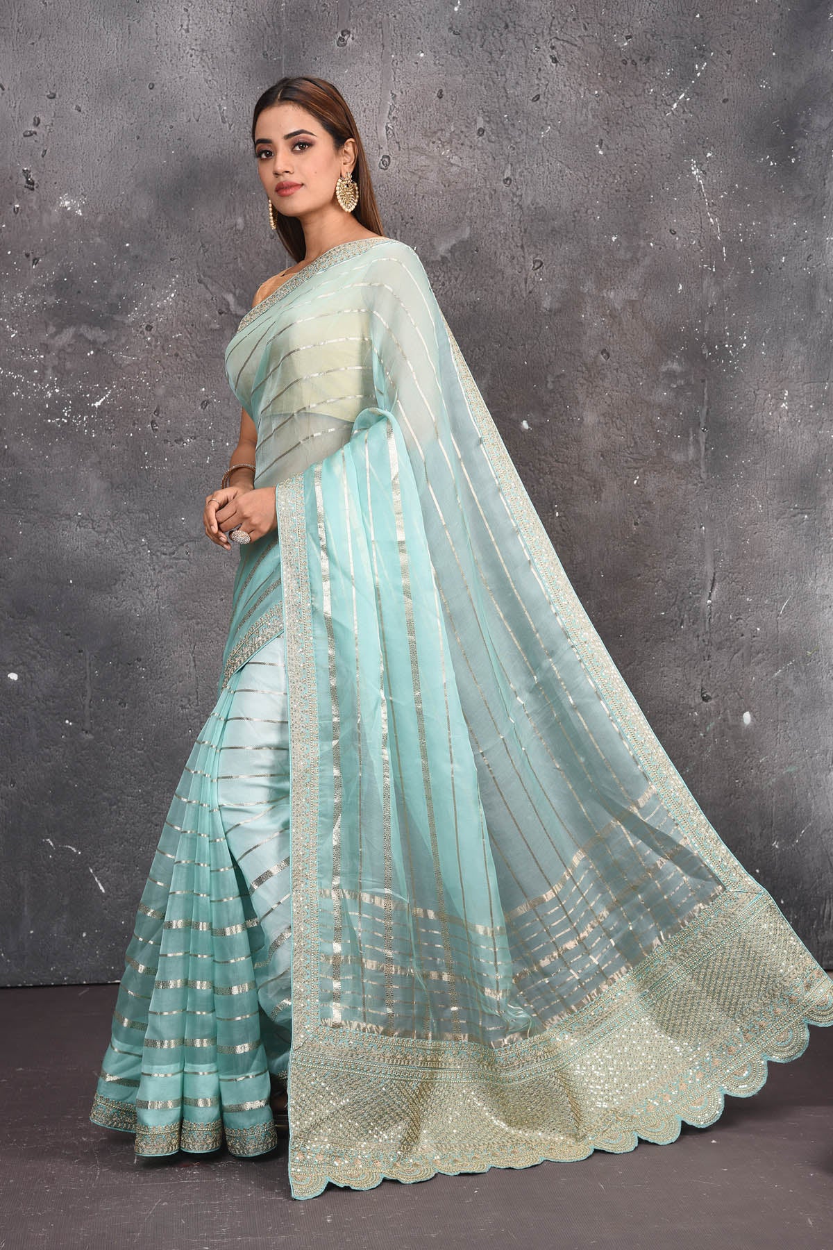 Buy this exquisite firozi blue saree in organza with striped print and silver embroidered border online in USA which is made of organza fabric and lightweight. This organza Saree is beautified with printed work and latest trend. Ideal for casual, kitty parties, stylish accessories. Shop this from Pure Elegance Indian fashion store in USA.- Side view.