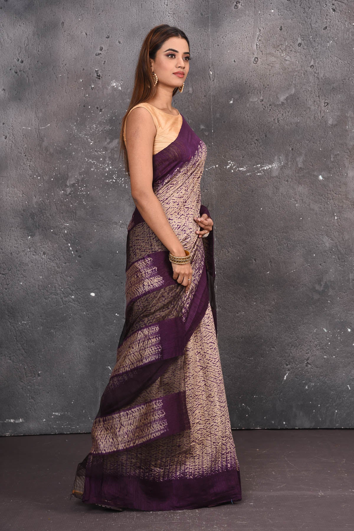 Shop this elegant purple-gold handloom shibori tussar saree online in USA which is handcrafted from fine silk tussar fabric, this tie and dye saree brings out the nature of flow. You can pair this beautiful shibori print with minimal jewellery for a casual day outfit. Add this plain shibori saree to your collection from Pure Elegance Indian fashion store in USA.-Side view.