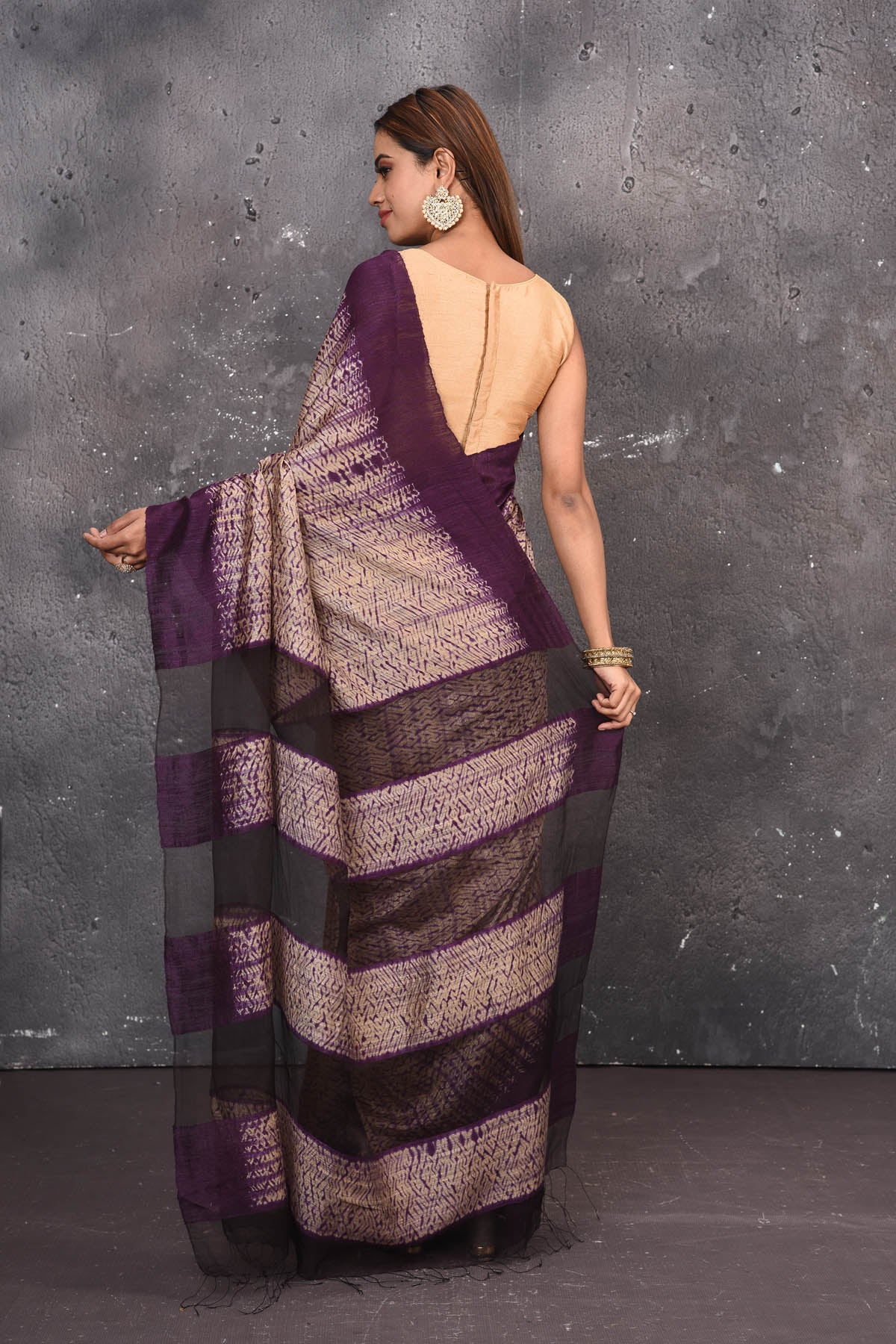 Shop this elegant purple-gold handloom shibori tussar saree online in USA which is handcrafted from fine silk tussar fabric, this tie and dye saree brings out the nature of flow. You can pair this beautiful shibori print with minimal jewellery for a casual day outfit. Add this plain shibori saree to your collection from Pure Elegance Indian fashion store in USA.-Back view with open pallu.