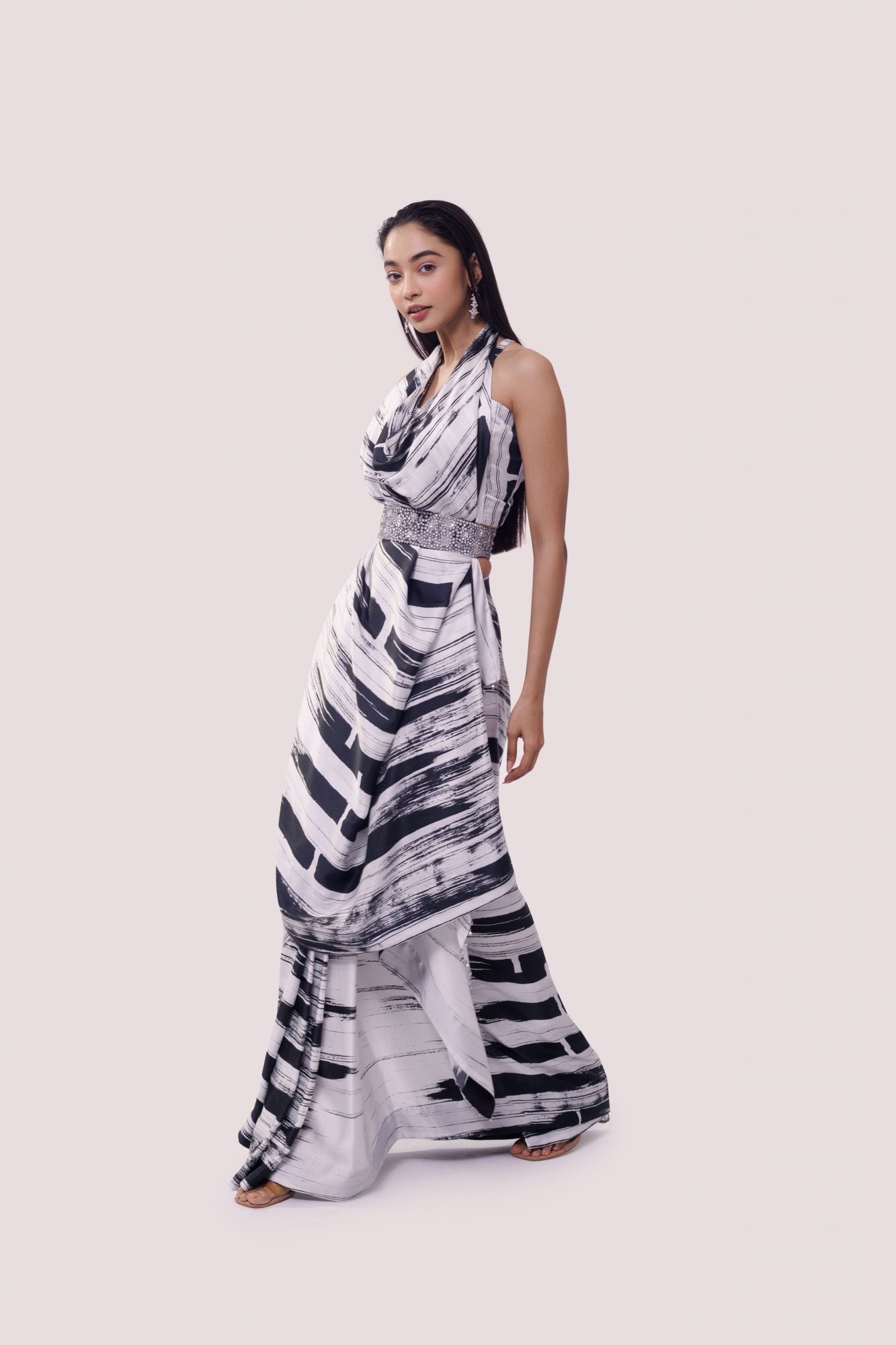 Shop a black & white striped printed georgette saree with stone, tikki, and dabka work, a strappy blouse, and belt detailing are a perfect choice for parties! It comes with a designer saree blouse. Make a fashion statement at weddings with stunning designer sarees, embroidered sarees with blouses, wedding sarees, and handloom sarees from Pure Elegance Indian fashion store in the USA.