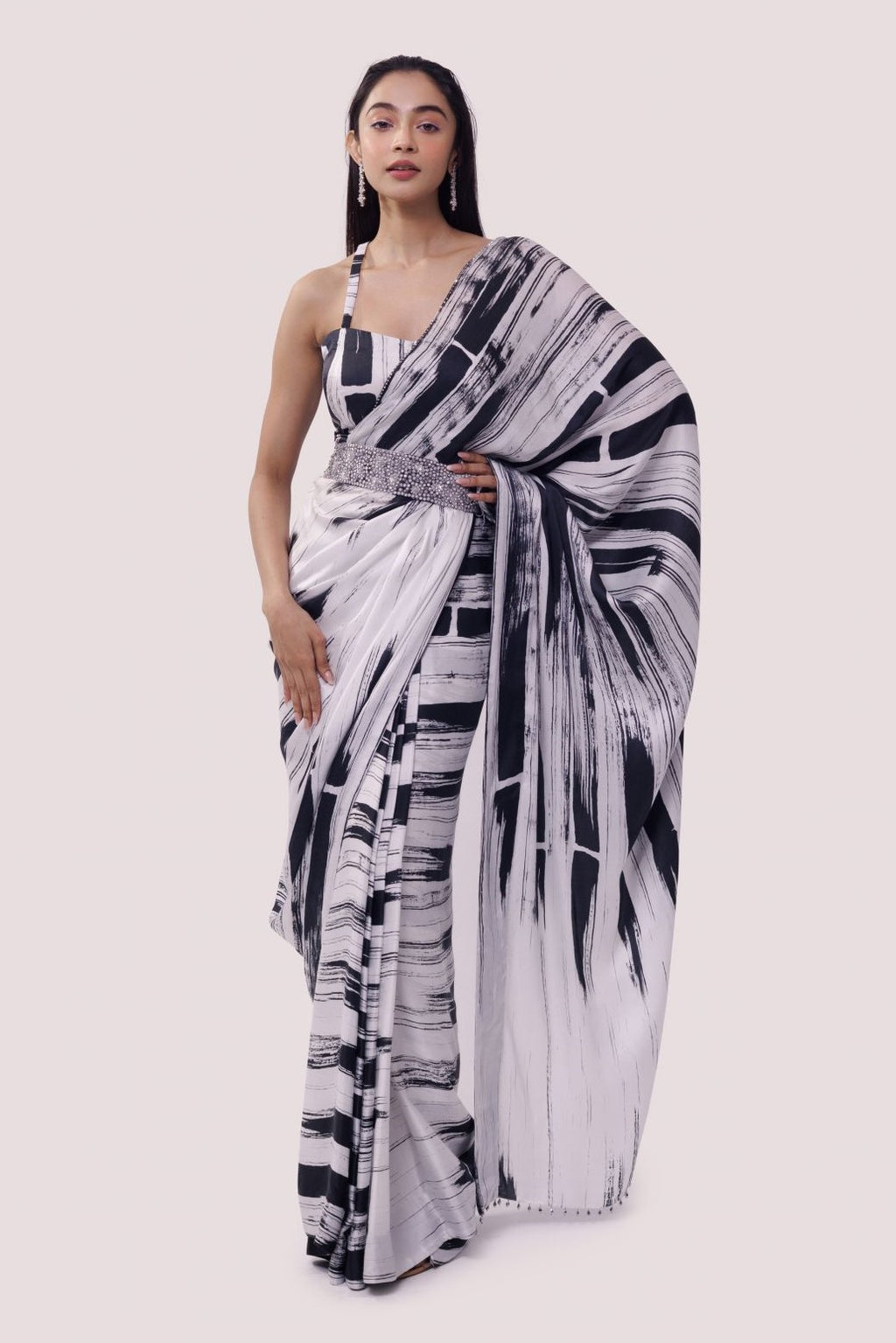 Shop a black & white striped printed georgette saree with stone, tikki, and dabka work, a strappy blouse, and belt detailing are a perfect choice for parties! It comes with a designer saree blouse. Make a fashion statement at weddings with stunning designer sarees, embroidered sarees with blouses, wedding sarees, and handloom sarees from Pure Elegance Indian fashion store in the USA.
